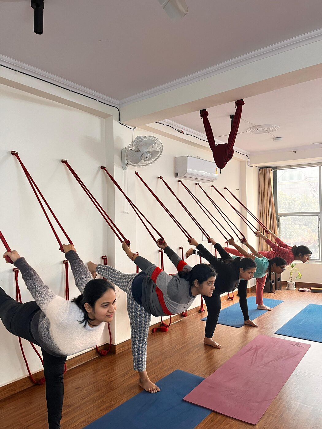 Students stretching using wall ropes in a guided group session at Veda Yoga Studio