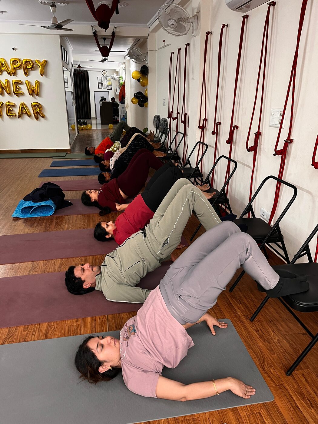 Students practising bridge pose with chair support during a festive batch session